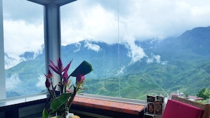 Een kamer met een groot raam dat uitkijkt over een bergachtig landschap.