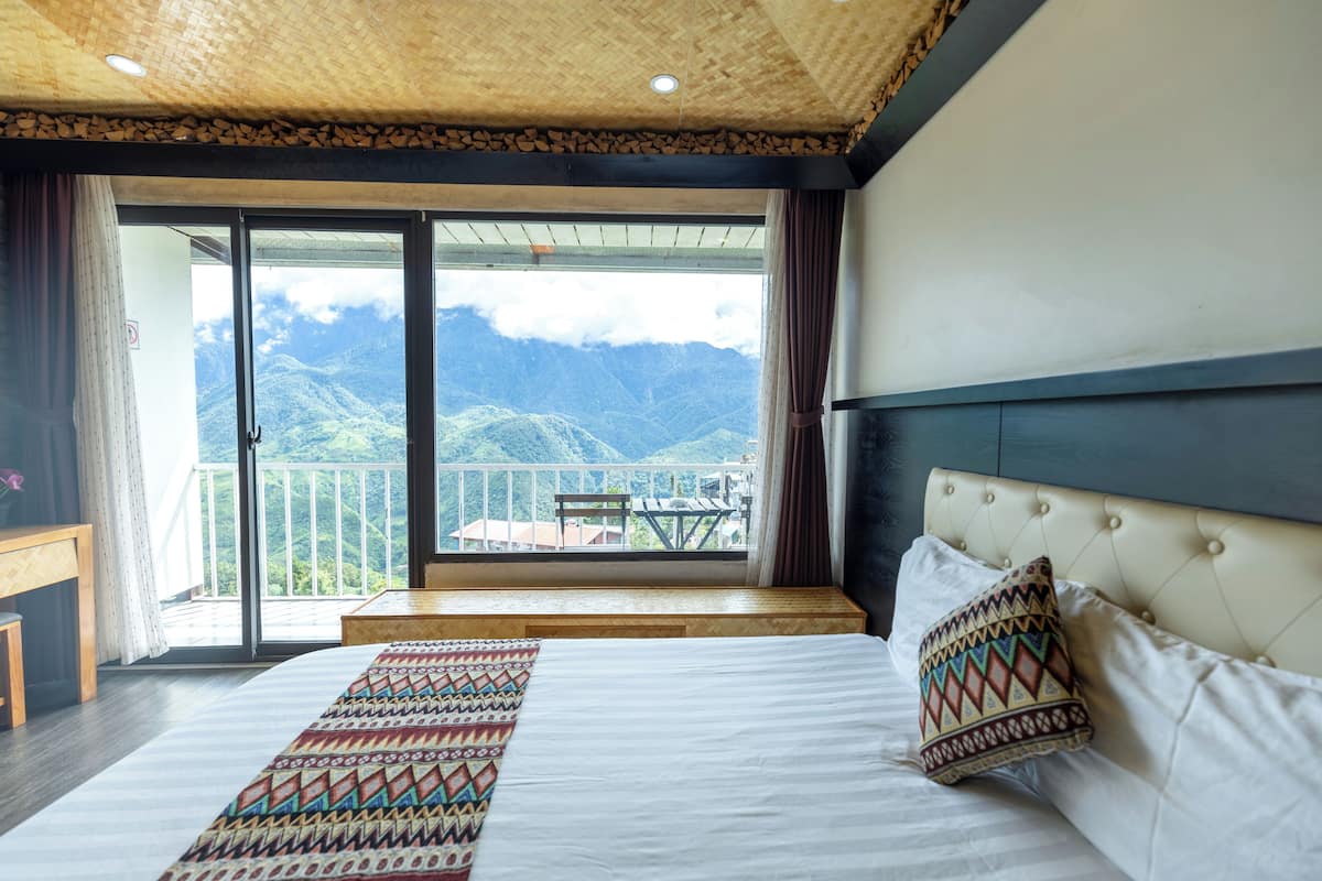 Een slaapkamer met een groot bed, uitzicht op bergen vanuit een balkon, en een houten plafond.
