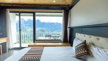 A bedroom with a large bed, a view of mountains through a balcony, and a wooden ceiling.
