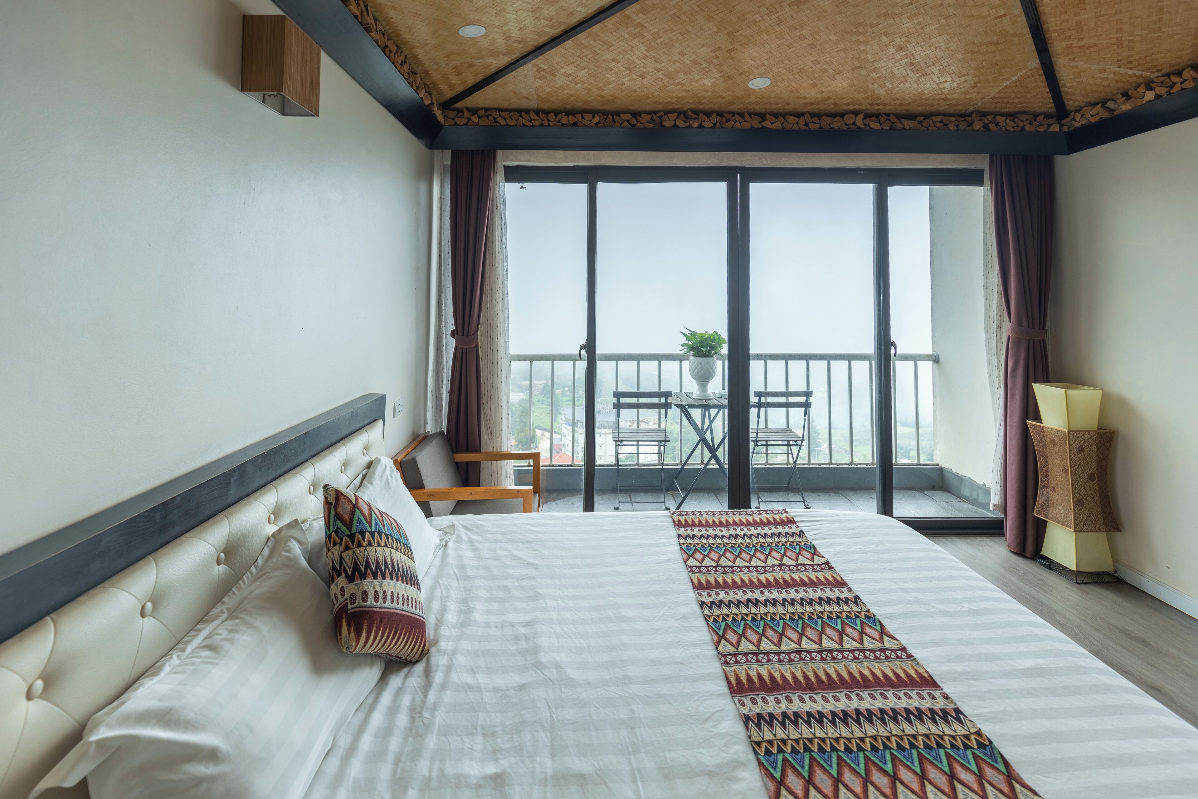 A hotel room with a large bed, a balcony with a table and chairs, and a view of the city.