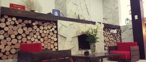 A lobby with a stone fireplace, wooden log display, and red seating.