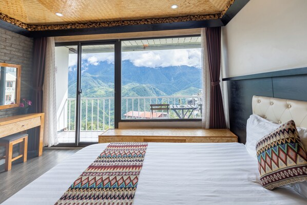 Een slaapkamer met een groot bed, een houten bureau en uitzicht op bergen door een schuifdeur van glas.