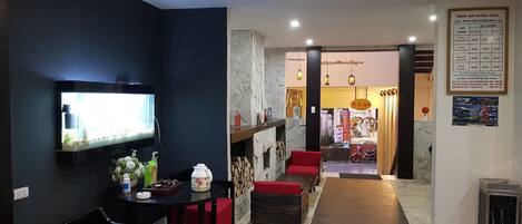 A modern interior with a TV mounted on the wall, a dining area with red chairs, a small table with a pitcher and cups, and a hallway leading to another room.