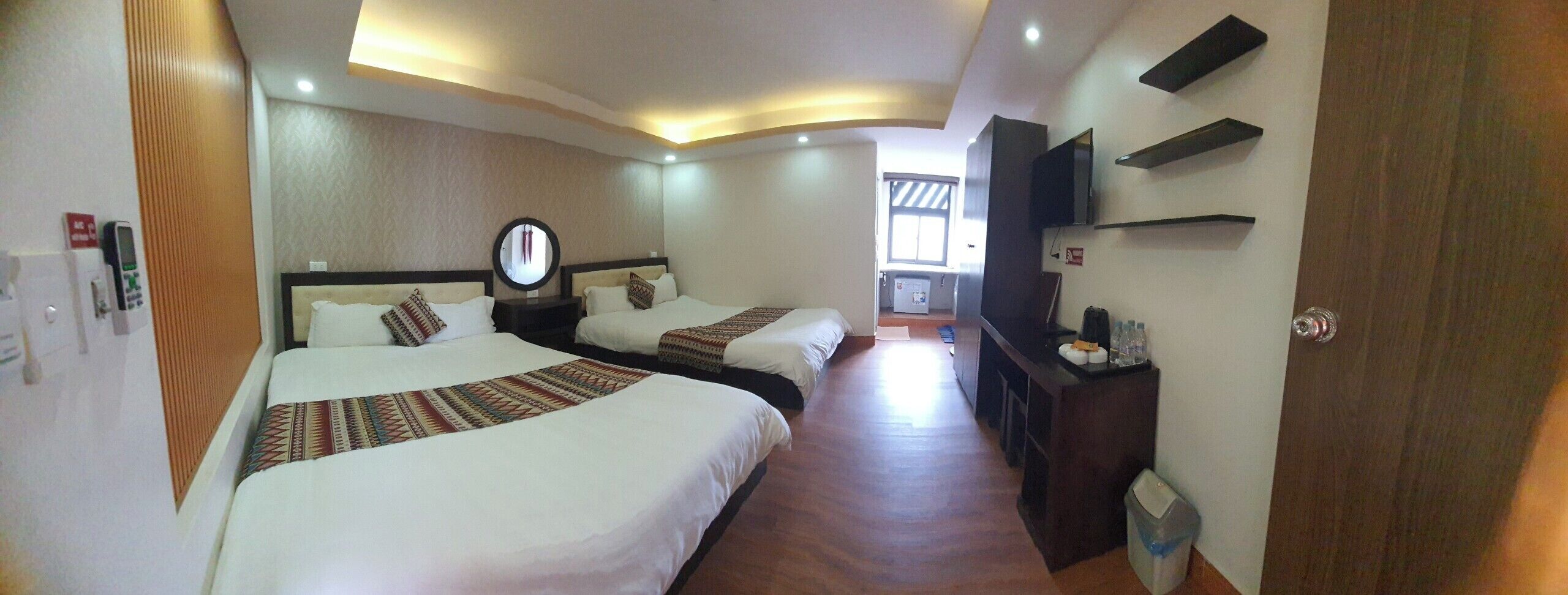 A hotel room with two beds, a mirror, a small desk, and a TV.