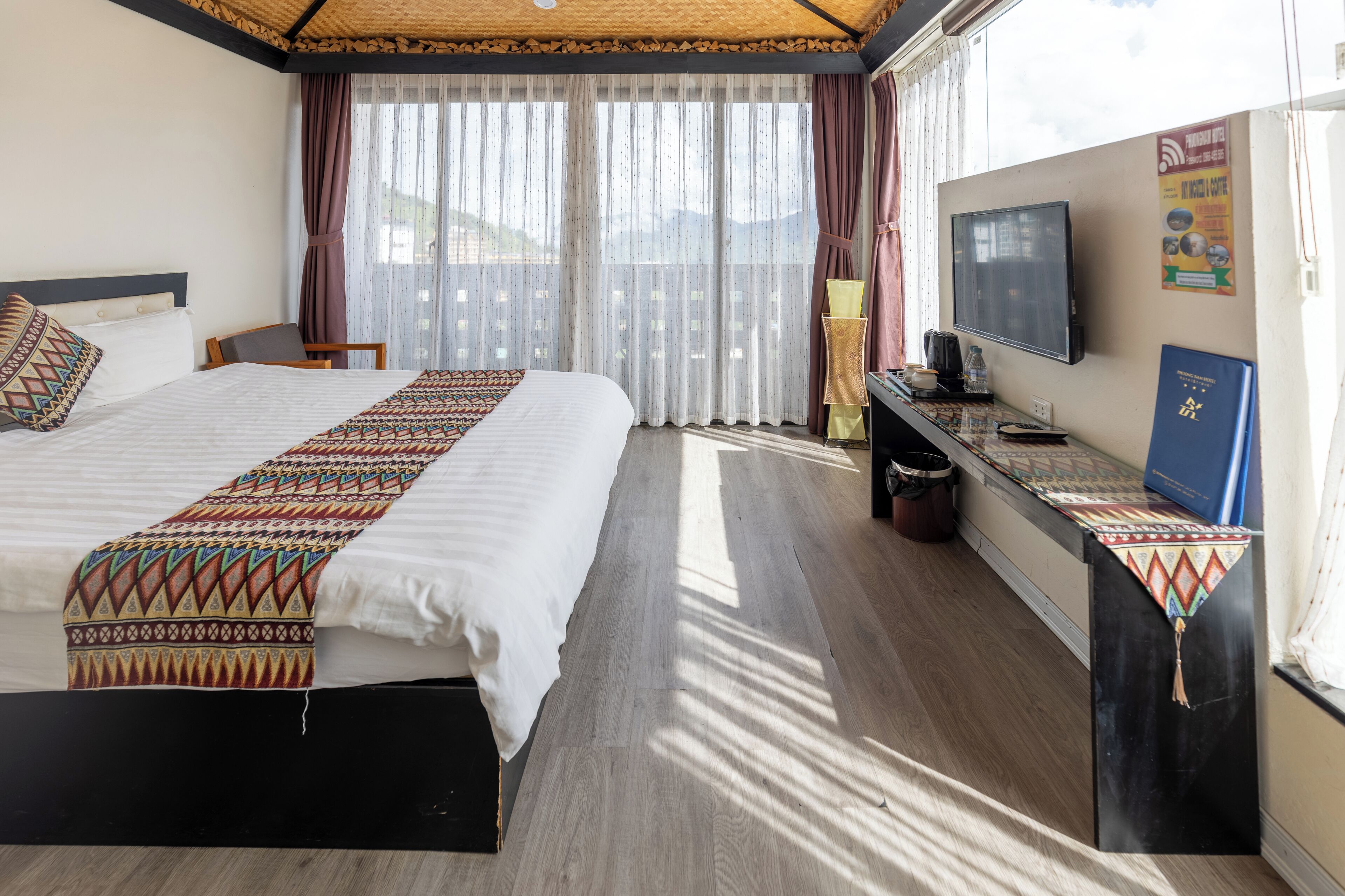 A hotel room with a large bed, a desk with a television, and a window with curtains.
