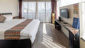 Een hotelkamer met een groot bed, een bureau met een televisie en een raam met gordijnen.