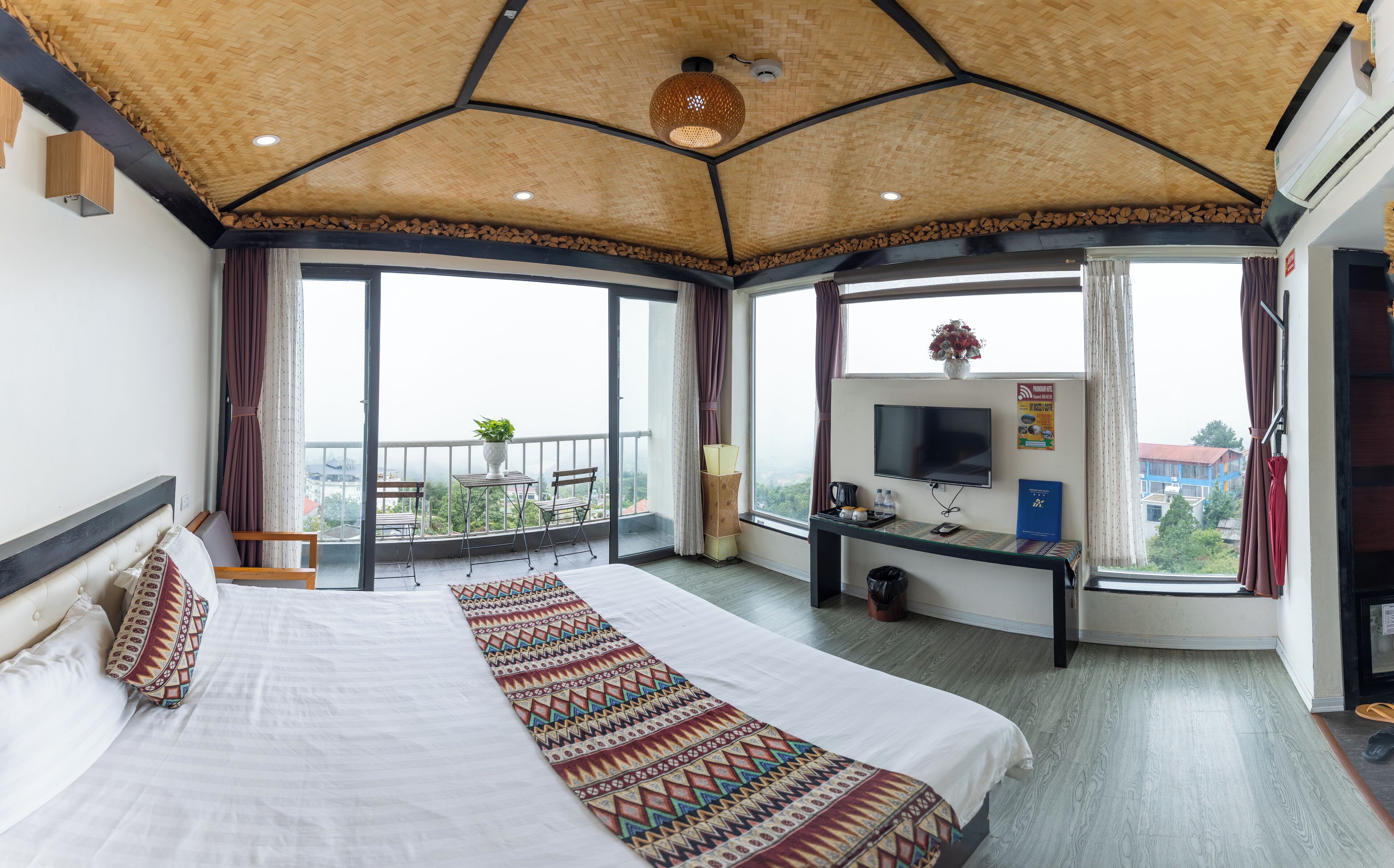 A hotel room with a large bed, a desk with a TV, and a balcony with a view.