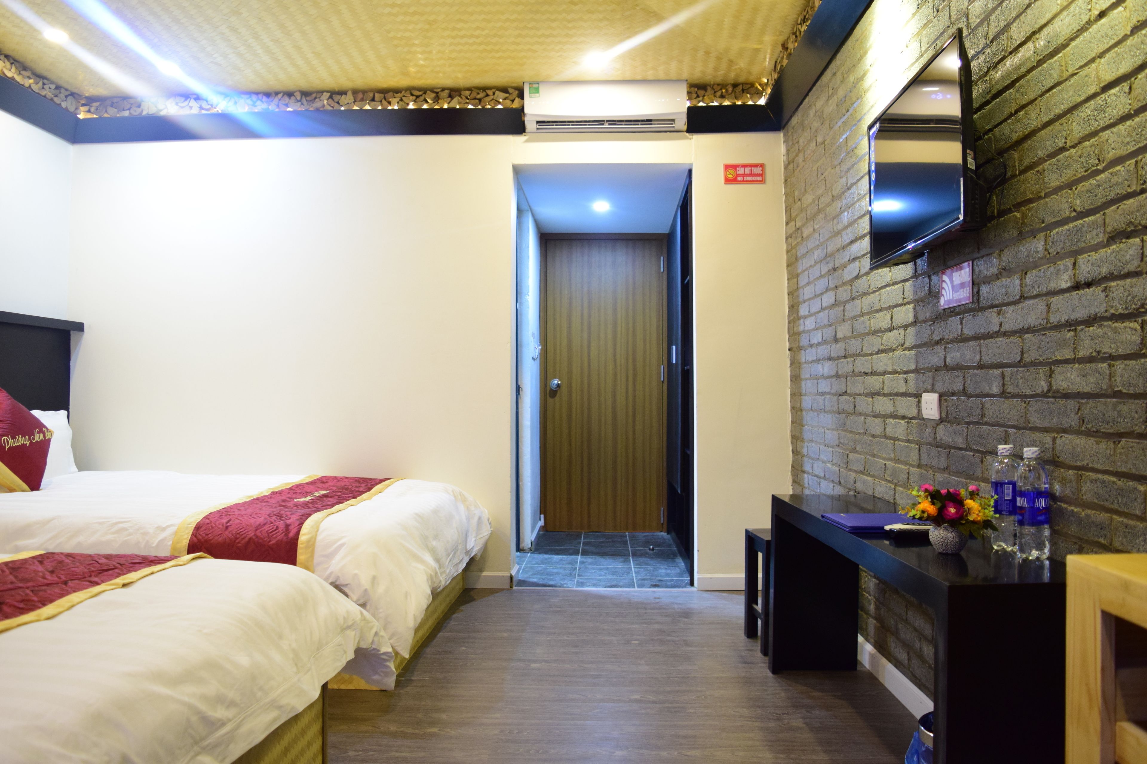 A hotel room with two beds, a desk with a mirror, and a brick wall.