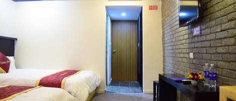 A hotel room with two beds, a desk with a mirror, and a brick wall.