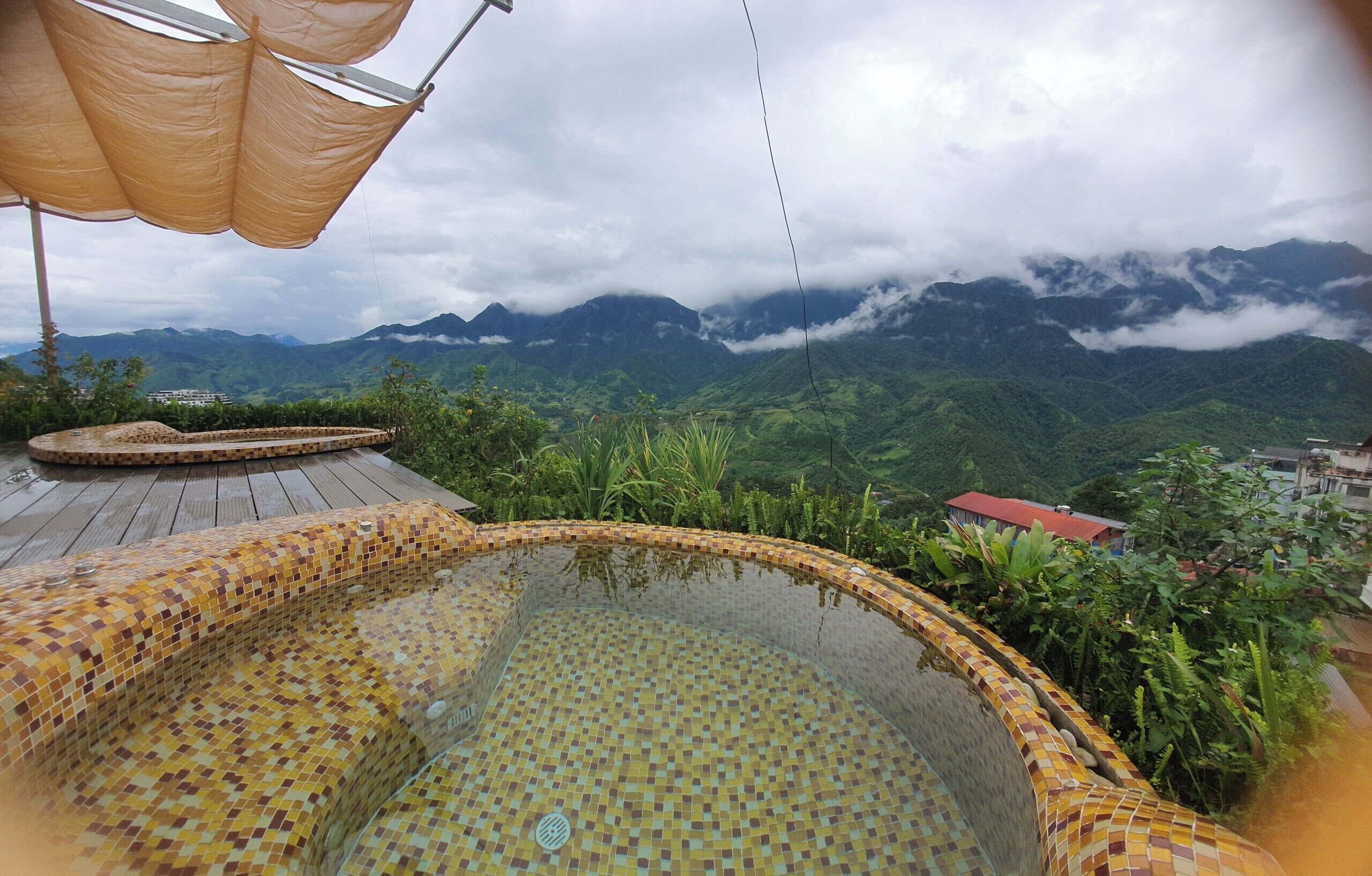Ein Whirlpool mit Mosaikfliesen, umgeben von üppiger Vegetation und einer Bergkulisse.