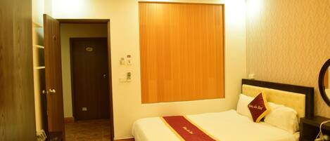 A hotel room with two beds, a wooden door, a wall-mounted light, and a small bedside table.