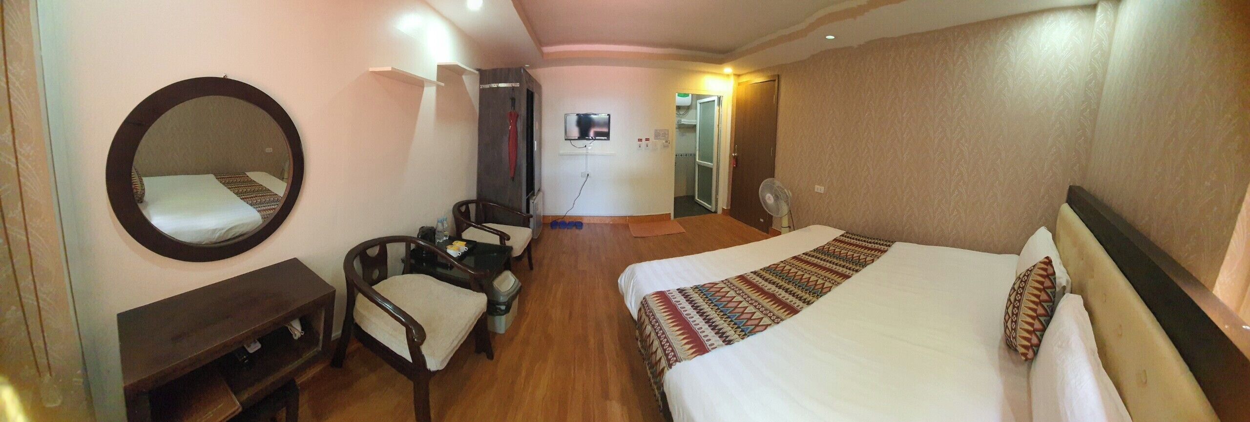 A hotel room with two beds, a desk, a chair, a mirror, a TV, and a shower area.