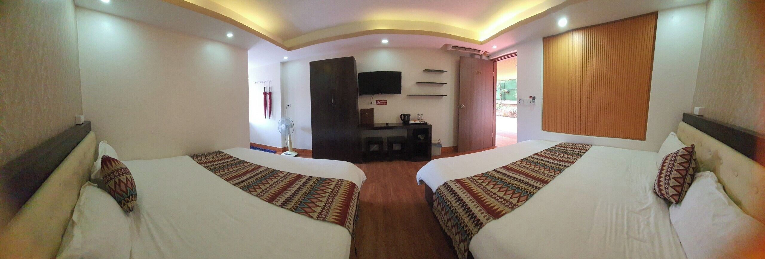 A hotel room with two beds, a desk, a television, and a window with curtains.