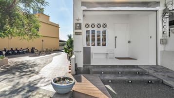 Una entrada de edificio con puerta blanca, un pequeño espacio de asientos al aire libre y una maceta grande con una flor.