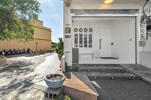 Una entrada de edificio con puerta blanca, un pequeño espacio de asientos al aire libre y una maceta grande con una flor.
