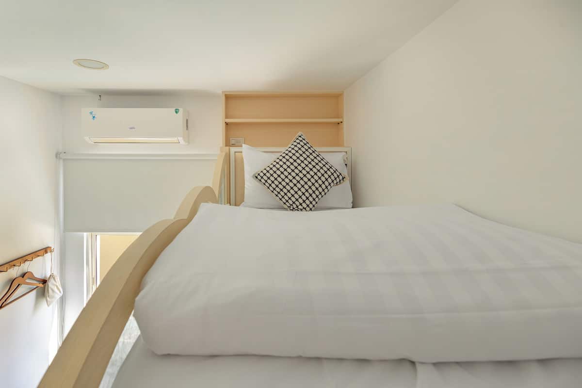 A bedroom with a bunk bed, a hanging light fixture, a wall-mounted air conditioner, and a wooden shelf above the bed.