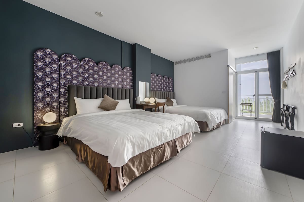 A modern bedroom with two beds, a large window, and a balcony.