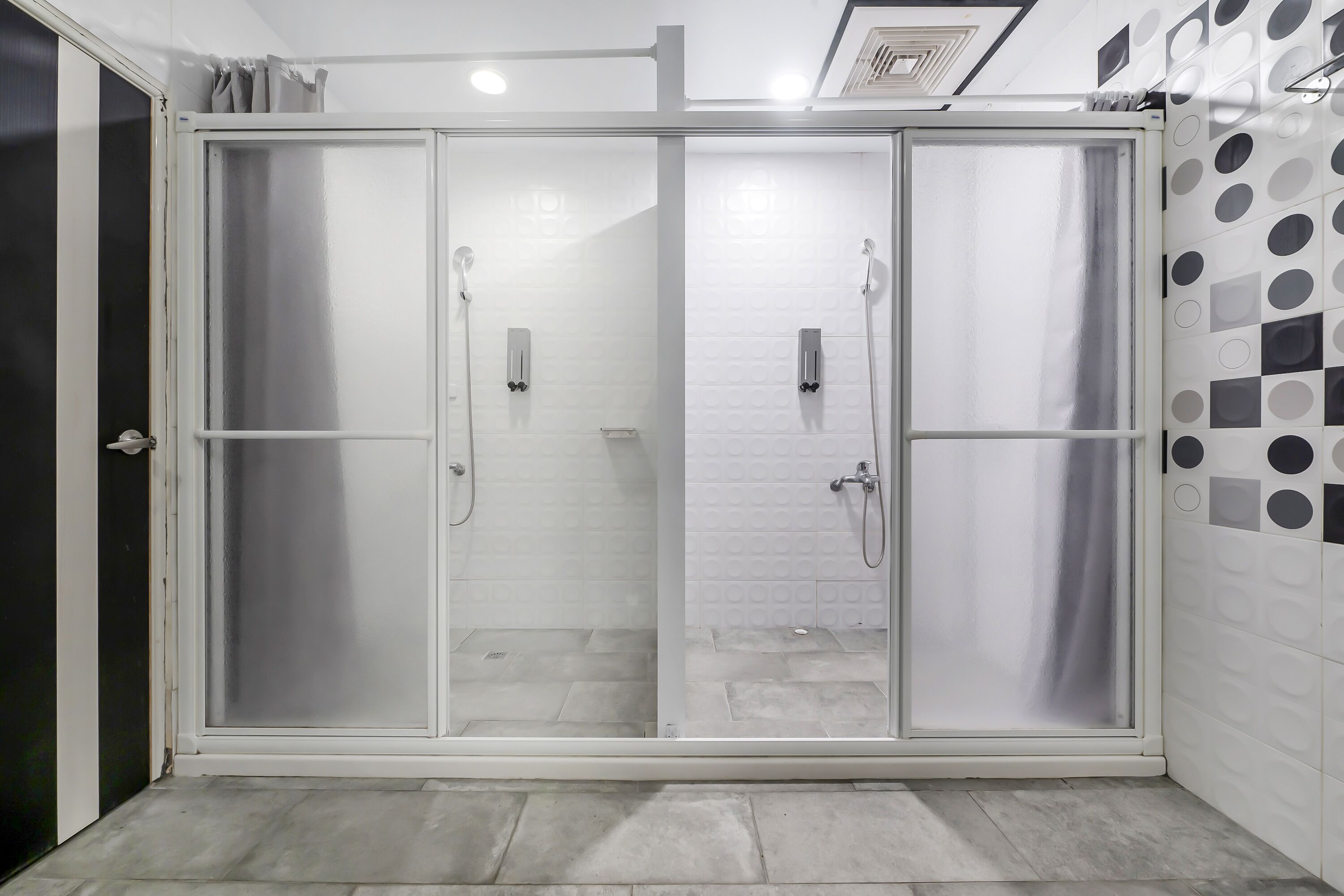 A glass-enclosed shower area with a tiled floor and a white tiled wall with a geometric pattern.