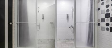 A glass-enclosed shower area with a tiled floor and a white tiled wall with a geometric pattern.