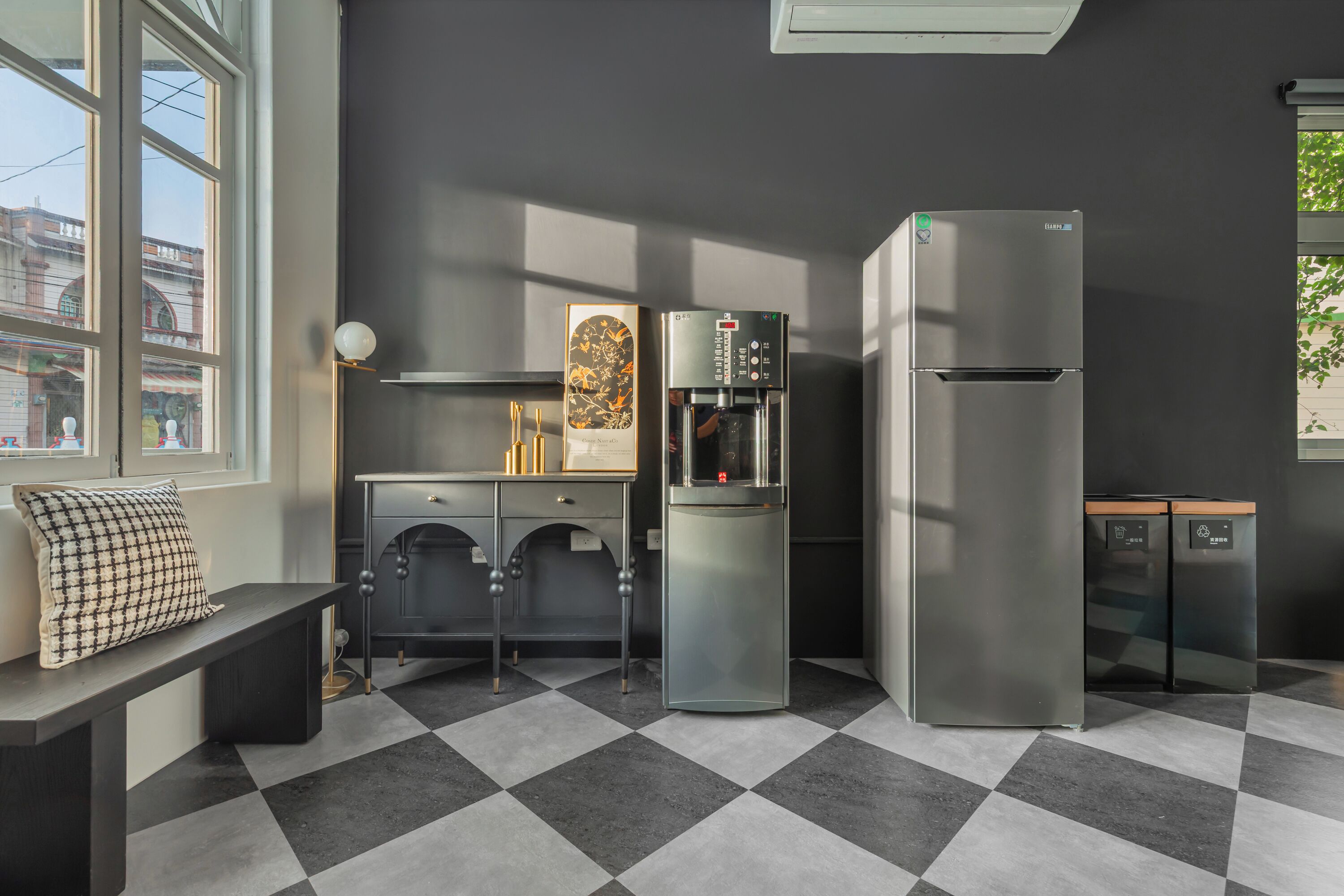 A modern kitchen with a checkered floor, a refrigerator, a water dispenser, and a bench with a pillow.