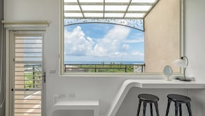 Un baño moderno con un ventanal amplio, un tocador blanco, dos taburetes negros y un espejo.