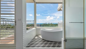Un baño moderno con una bañera independiente, cabina de ducha con paredes de vidrio y vista al océano a través de un ventanal grande.
