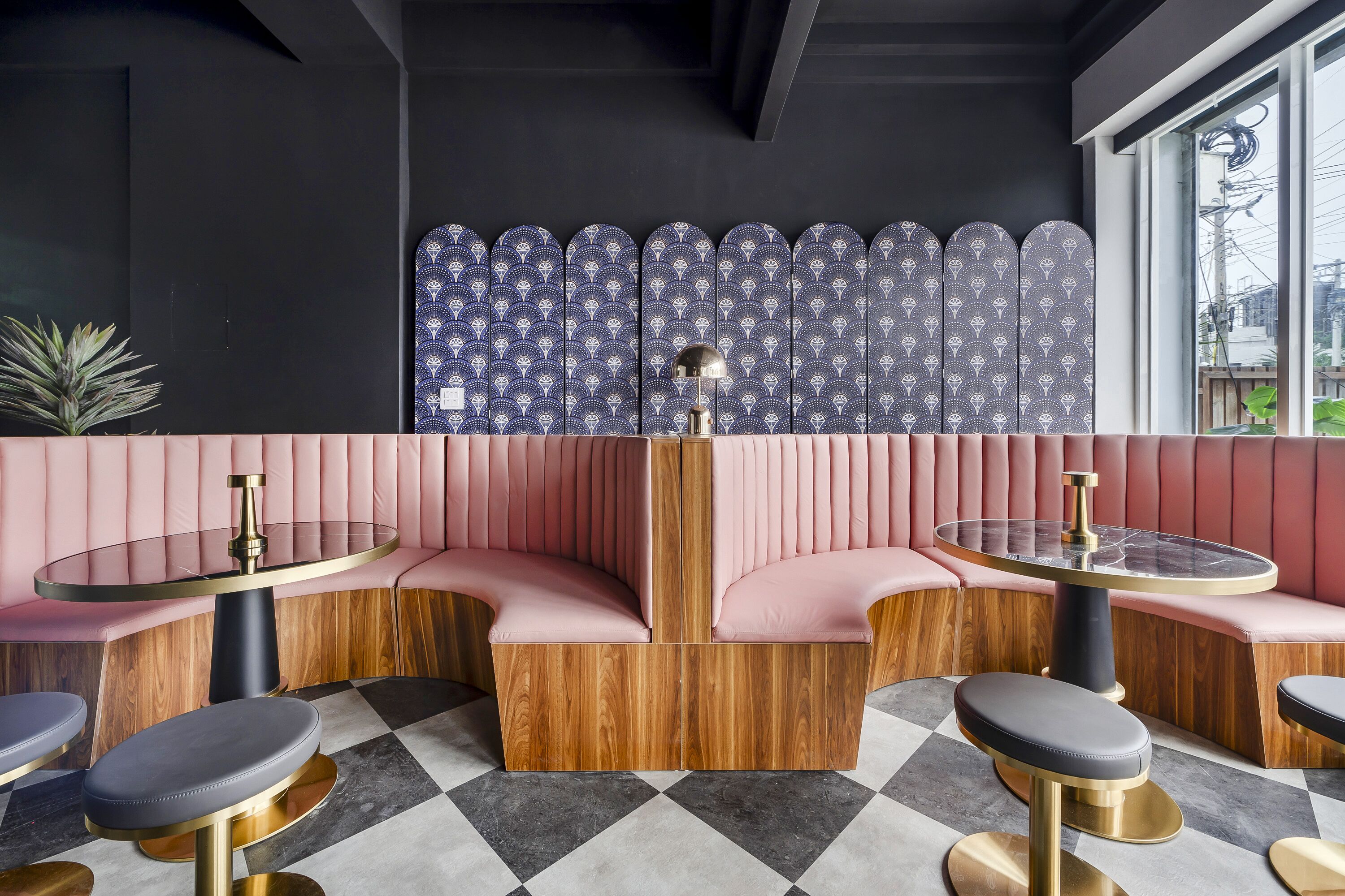 Un interior moderno con un banco acolchado rosa, mesas de madera y una pared con estampado.