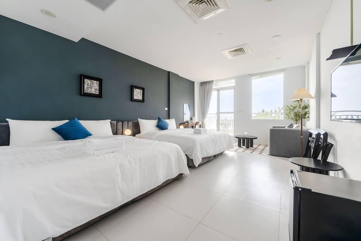 A modern hotel room with two beds, a desk, and a large window offering a view.