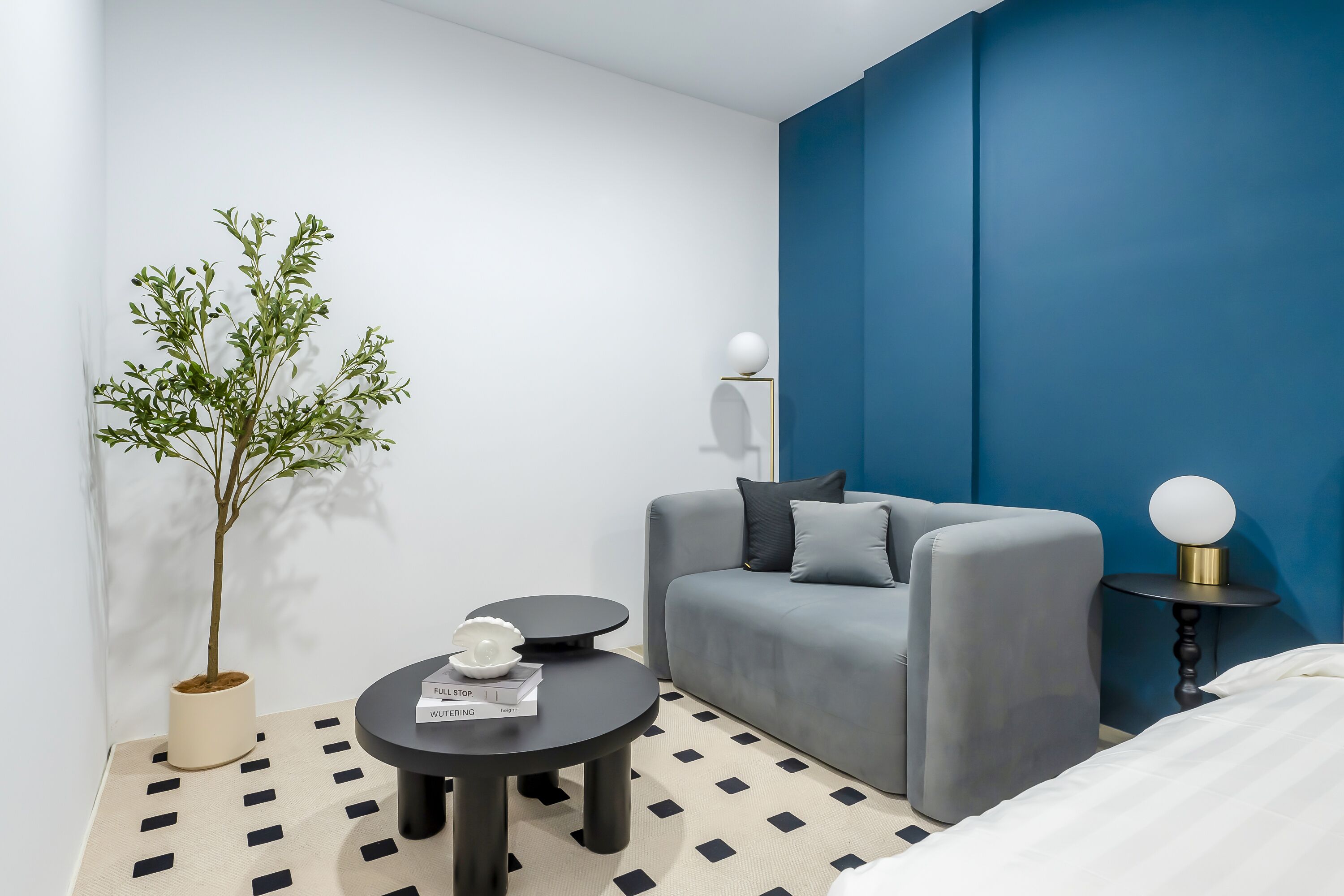 A modern room with a grey sofa, a small round table with a book, a potted plant, and a blue accent wall.