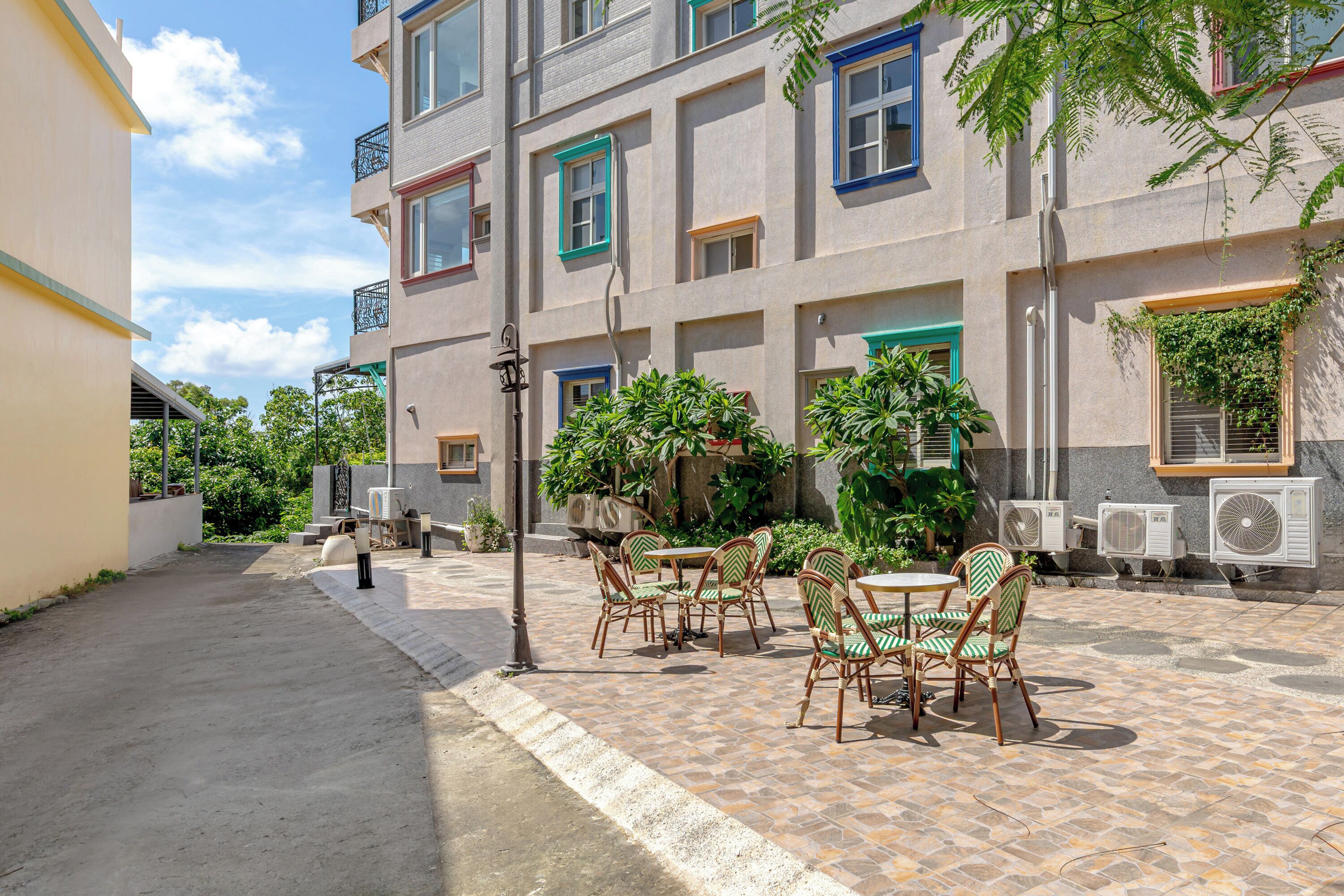 Une cour dotée d’un espace extérieur aménagé avec des sièges, de climatiseurs et d’un bâtiment aux fenêtres aux encadrements colorés.