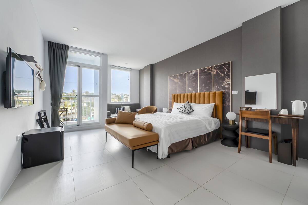 A modern hotel room with a large bed, a desk, and a sofa.
