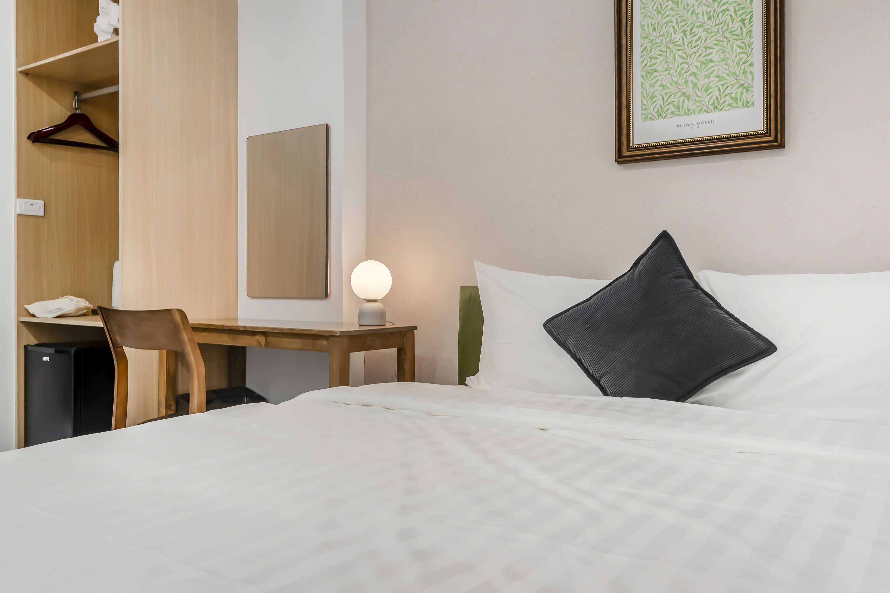 Una habitación de hotel con cama, escritorio, silla, armario y mesita de noche con lámpara.