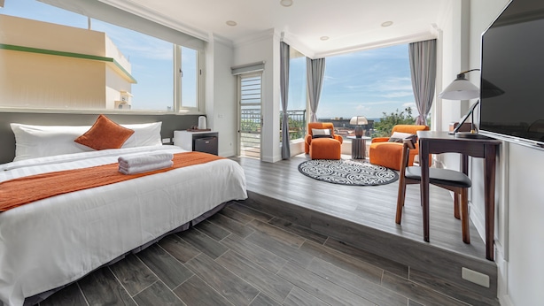 Habitación de hotel moderna con una cama grande, un escritorio con silla, televisor y un balcón con asientos.