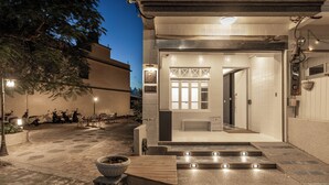 Un edificio con una entrada bien iluminada, un pequeño espacio de asientos al aire libre y una puerta visible que da al interior.