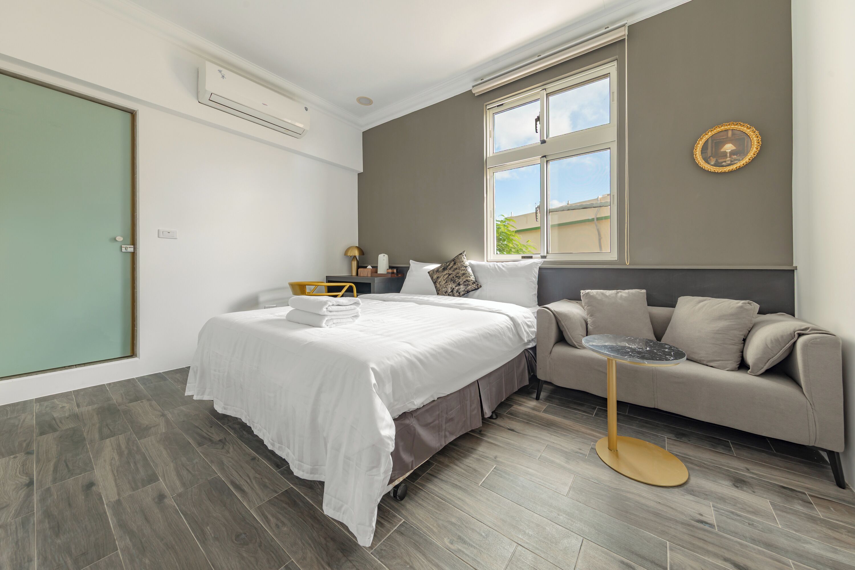 Quarto moderno com cama, sofá, mesa redonda pequena e janela.