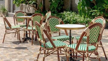 Sedie in vimini con cuscini a motivi verdi e bianchi, disposte attorno a un tavolo rotondo su un patio in pietra.