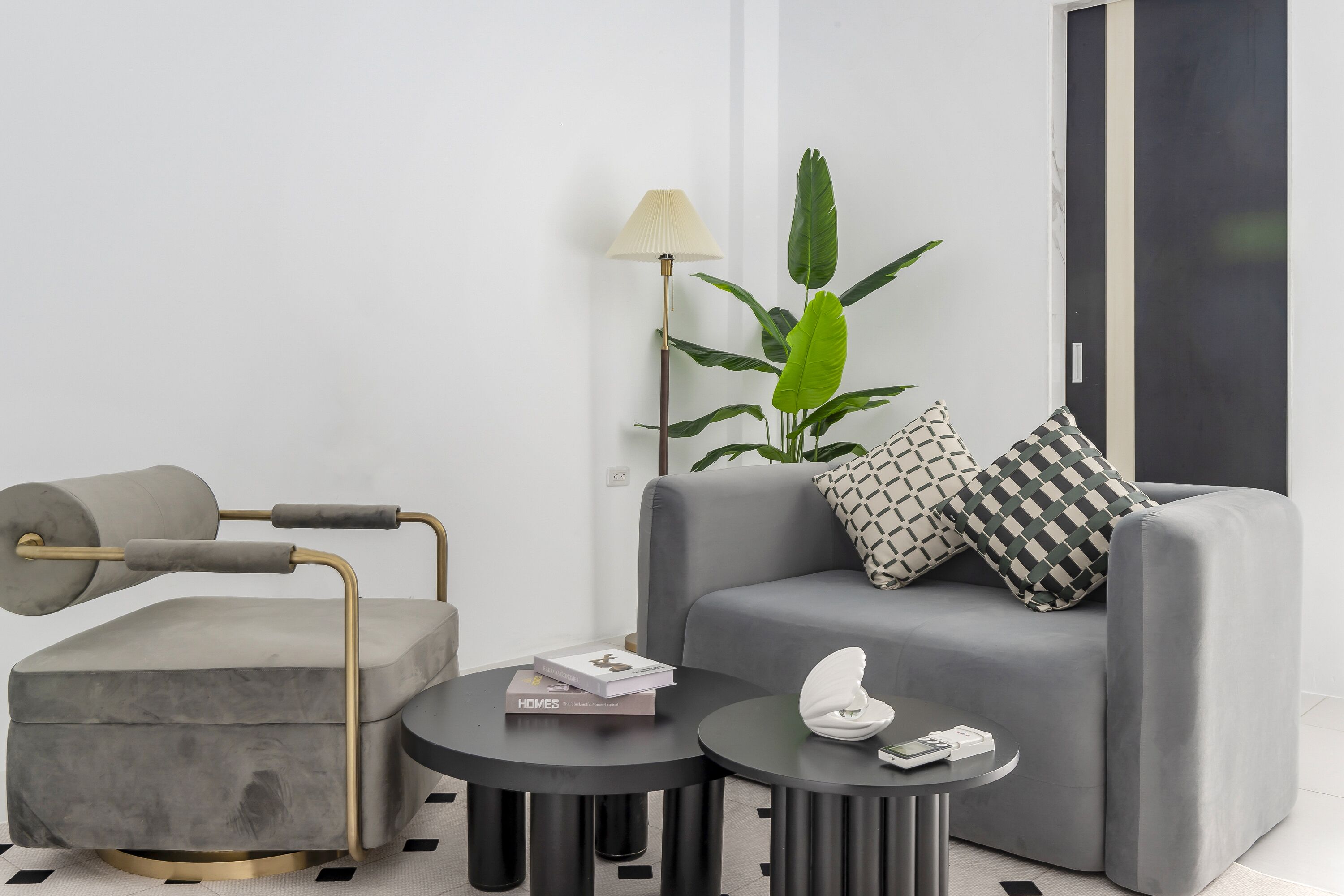 Una sala moderna con un sofá gris, una mesita redonda pequeña, un sillón gris y una lámpara de pie.