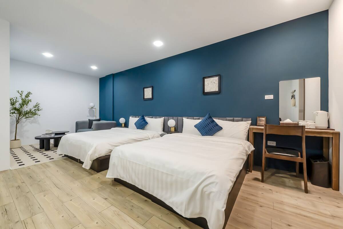 A modern hotel room with two beds, a desk, and a chair.