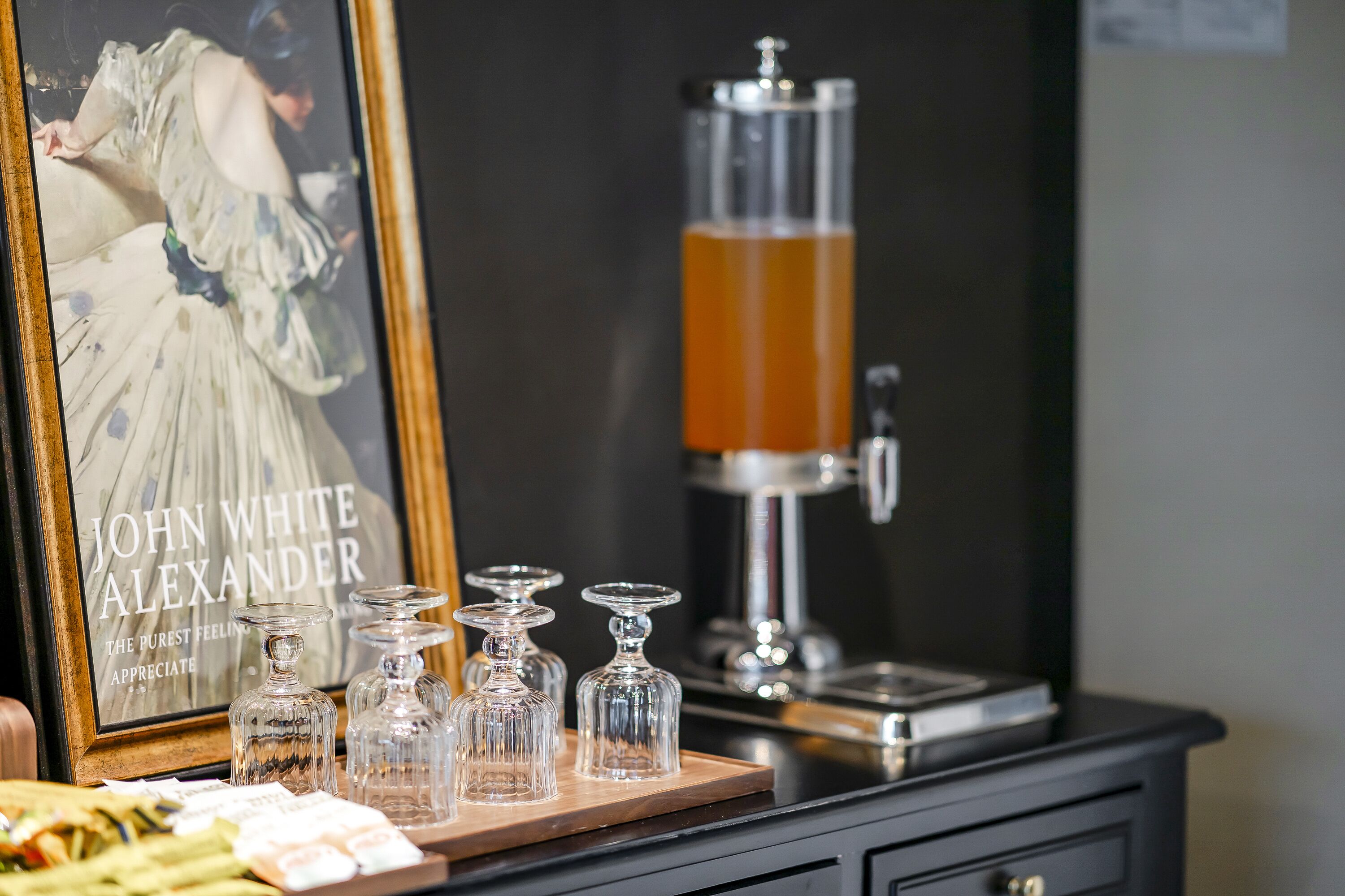 A bar area with a framed poster, a coffee machine, and several glass decanters on a wooden tray.