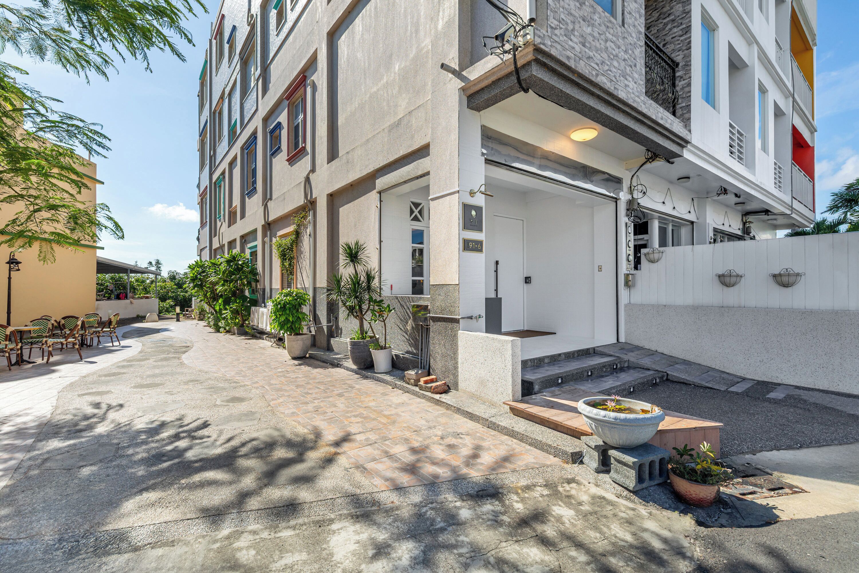 Un edificio moderno con acceso cubierto, mesas al aire libre y plantas en macetas.