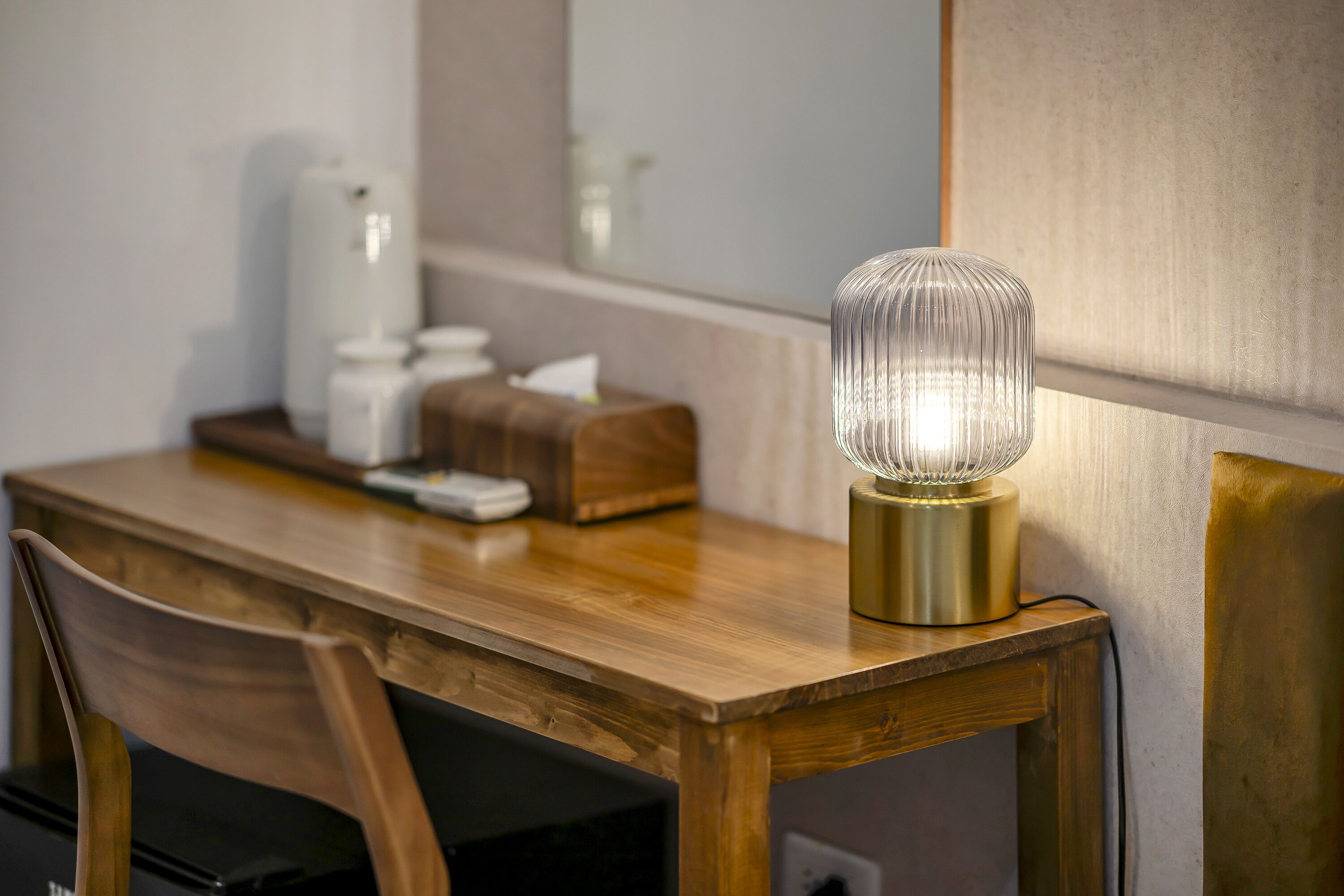 Een houten bureau met een lamp, een zakdoosje en een koffiezetapparaat.