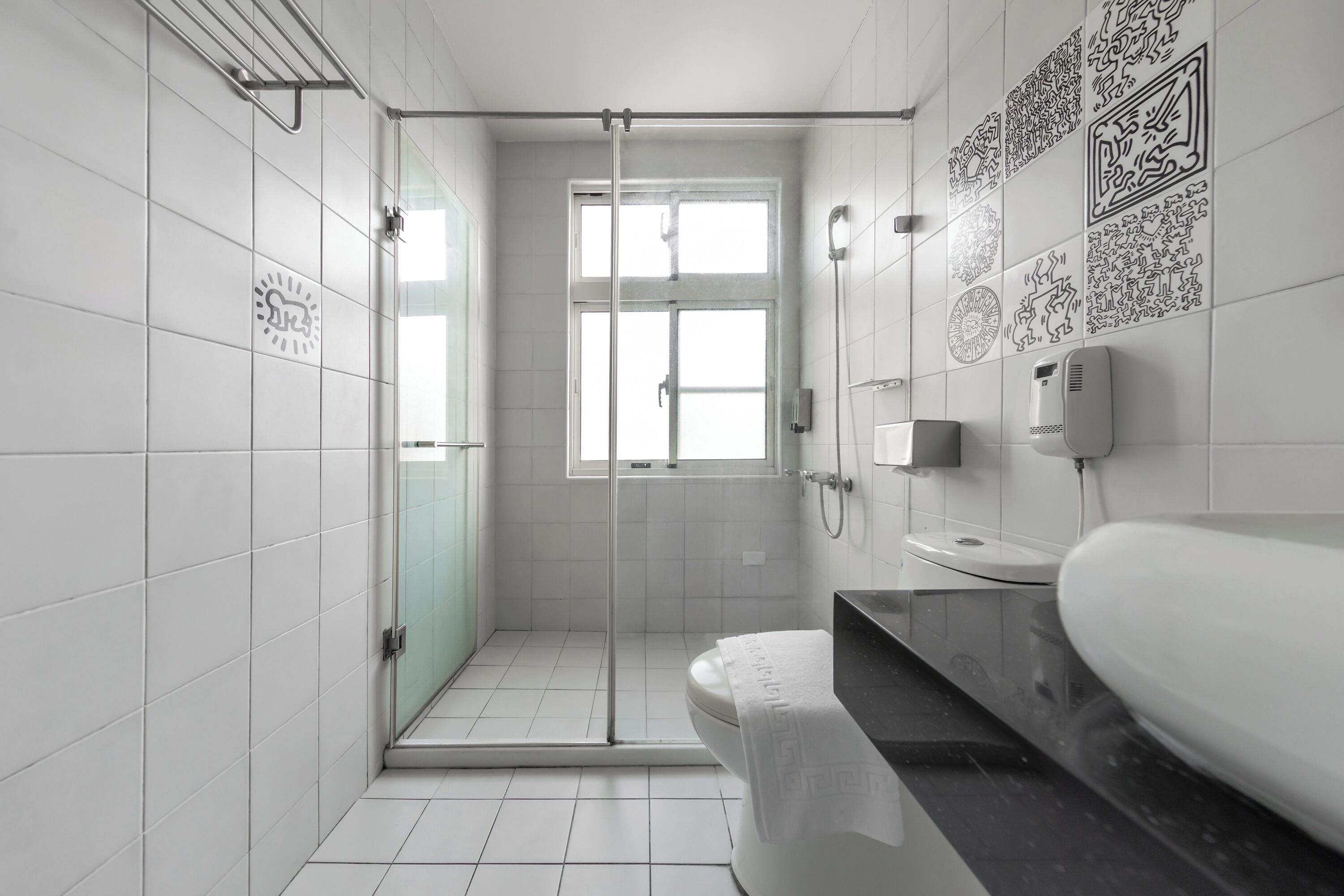 A modern bathroom with white tiles, a glass shower enclosure, a toilet, and a sink with a black countertop.