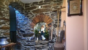 Un arc en pierre rustique mène à une petite pièce où se trouvent une charrette en bois, un grand pot et une cheminée rustique.