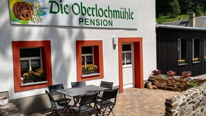 Un bâtiment sur lequel on peut lire l’inscription « Die Oberlochmühle Pension », et une terrasse avec une table et des chaises.
