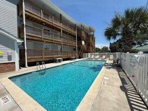 A rectangular swimming pool with a wooden deck and a white fence.