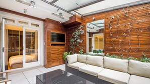 A modern living room with a glass coffee table, a beige sofa, and a wooden wall with climbing plants. - Central London Apartment, near Victoria Station (London)
