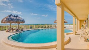 Zona de piscina con vista al océano, sillas de descanso y sombrillas de paja.