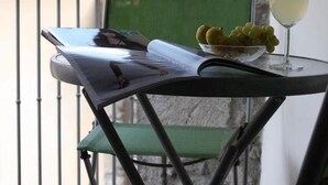 A balcony with a table, a chair, a bowl of grapes, and a glass of white wine. - Il Lupo Rosso (Santu Lussurgiu)