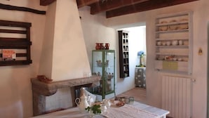 A cozy kitchen with a stone fireplace, a dining table set with white tableware, and shelves with dishes and ceramics. - Il Lupo Rosso (Santu Lussurgiu)