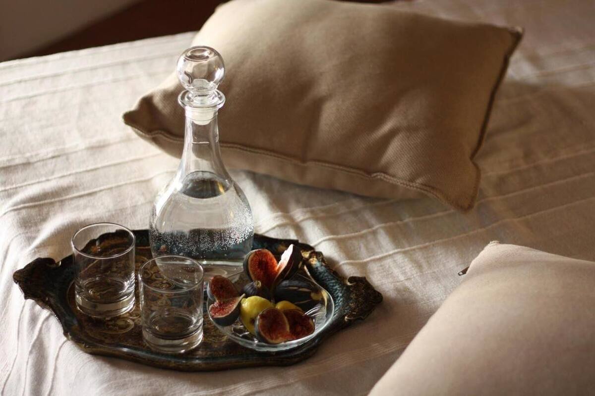 A tray with a decanter, glasses, and figs on a bed with pillows.